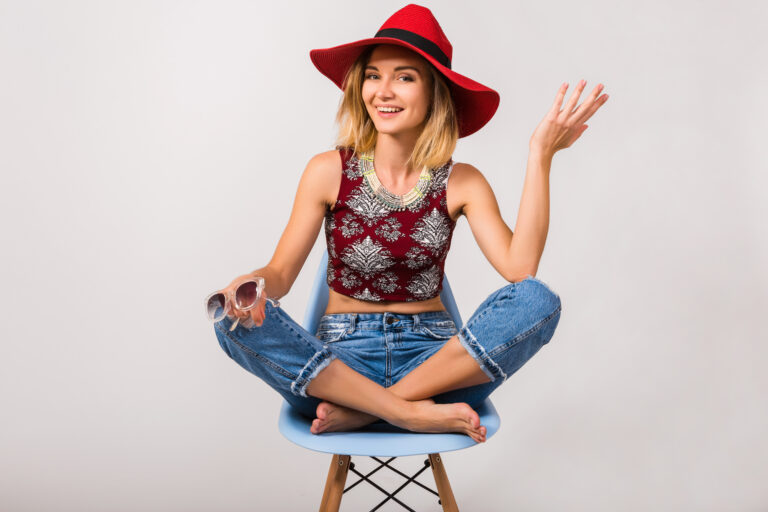 young hipster beautiful woman sitting on chair, isolated, jeans, top, summer vacation style, red hat, happy, positive, smiling, sunglasses, emotional, gesture, laughing